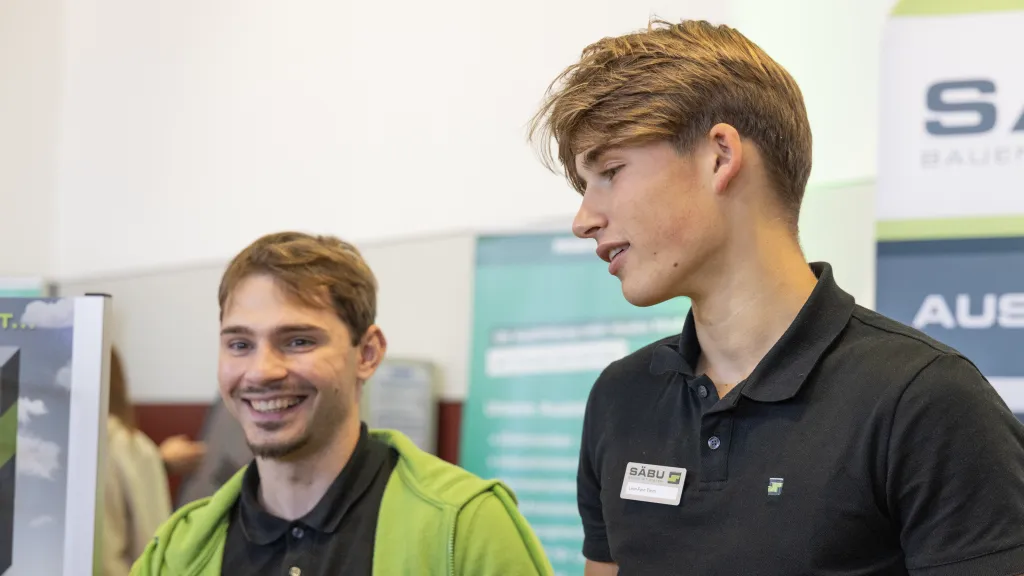 Zwei Azubis in Aktion die Spaß haben während sie mit den Schülerinnen und Schülern der Leonardo da Vinci Schule in Morsbach auf der Ausbildungsmesse sprechen.